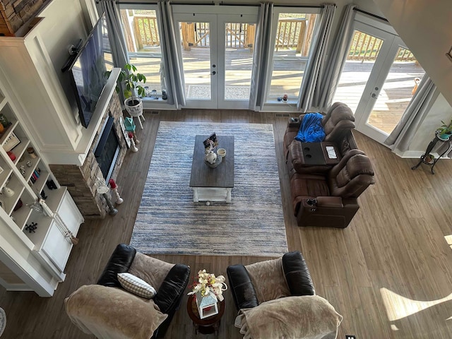 living room featuring built in features, a stone fireplace, wood-type flooring, and french doors