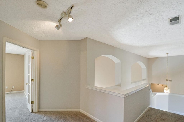 corridor with light colored carpet, track lighting, and a textured ceiling