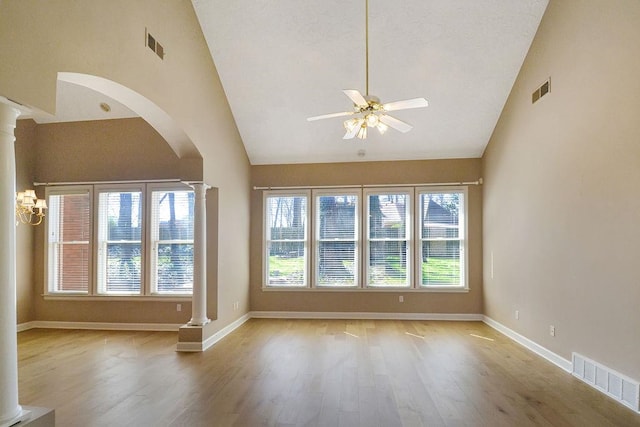 empty room featuring ceiling fan with notable chandelier, light hardwood / wood-style floors, high vaulted ceiling, and decorative columns