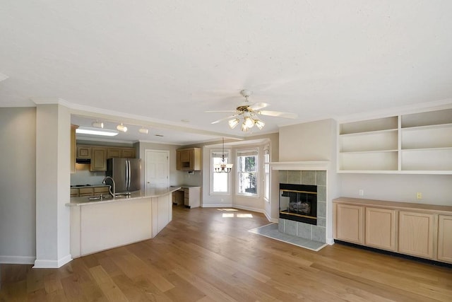 unfurnished living room with light wood-type flooring, ceiling fan, a tile fireplace, and sink