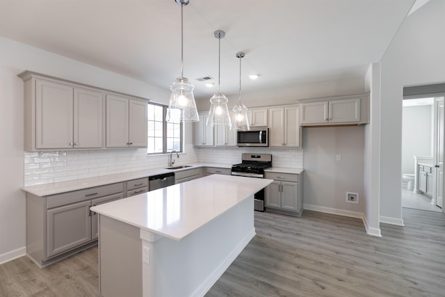 kitchen featuring appliances with stainless steel finishes, sink, a kitchen island, gray cabinets, and tasteful backsplash