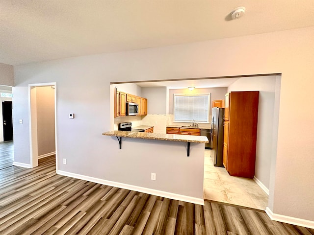 kitchen featuring appliances with stainless steel finishes, light stone counters, light hardwood / wood-style floors, kitchen peninsula, and a kitchen breakfast bar