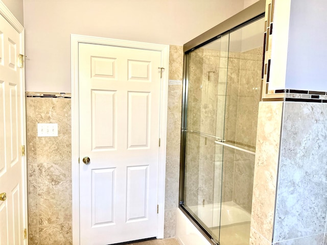 bathroom with tile walls and bath / shower combo with glass door