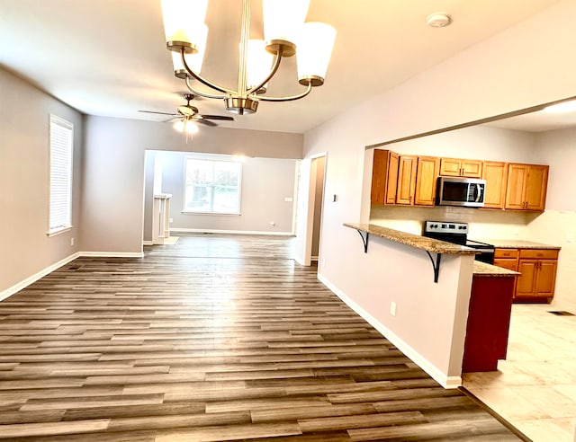 kitchen featuring dark hardwood / wood-style flooring, stainless steel appliances, pendant lighting, ceiling fan with notable chandelier, and a kitchen breakfast bar