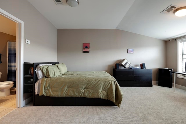 bedroom with ensuite bathroom, light carpet, and lofted ceiling