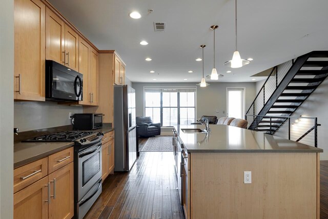 kitchen with sink, an island with sink, stainless steel appliances, pendant lighting, and dark hardwood / wood-style floors