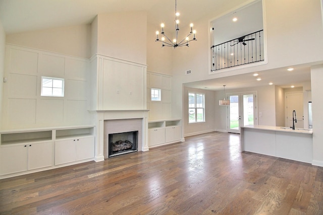 unfurnished living room featuring wood-type flooring, a notable chandelier, sink, and high vaulted ceiling