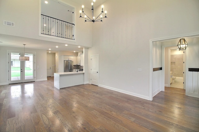 unfurnished living room with a high ceiling, a chandelier, and wood-type flooring