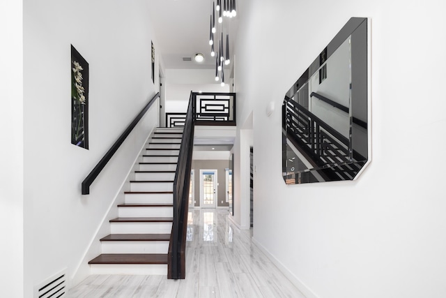 hallway featuring stairs, a towering ceiling, visible vents, and baseboards