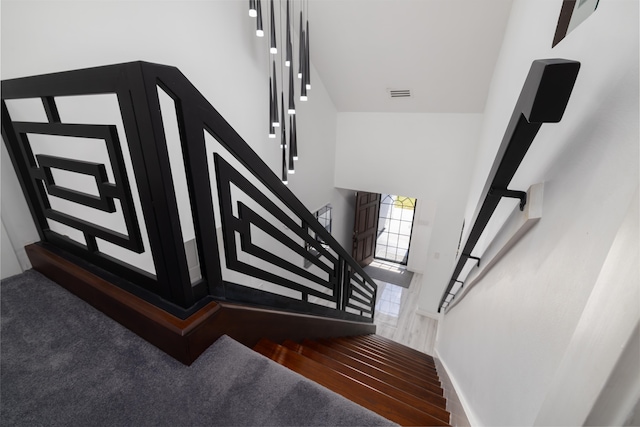 stairway with visible vents, a towering ceiling, baseboards, and wood finished floors