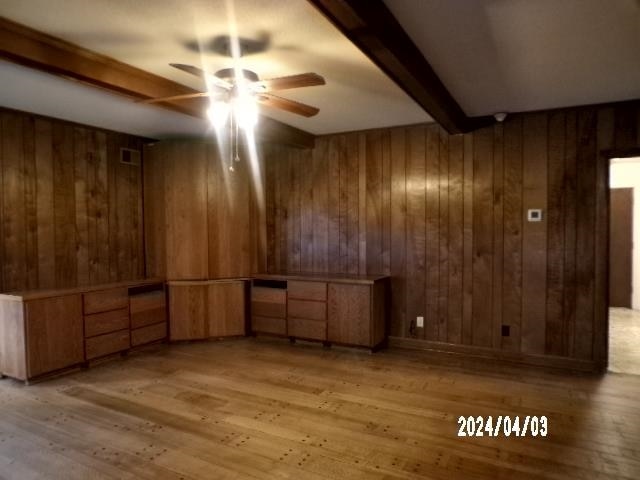 unfurnished room with beamed ceiling, light hardwood / wood-style floors, ceiling fan, and wood walls