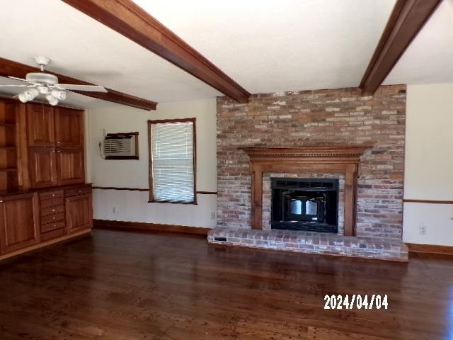 unfurnished living room featuring dark hardwood / wood-style flooring, ceiling fan, a brick fireplace, and beam ceiling