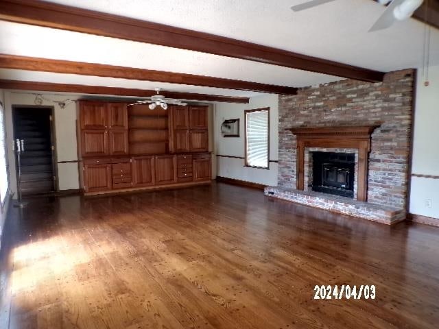 unfurnished living room with beamed ceiling, ceiling fan, dark hardwood / wood-style floors, and a brick fireplace