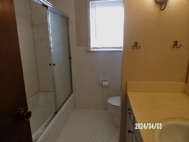 full bathroom with tile walls, toilet, tile floors, vanity, and bath / shower combo with glass door