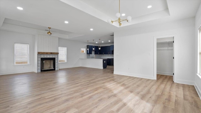 unfurnished living room with light hardwood / wood-style flooring, a tray ceiling, and ceiling fan with notable chandelier