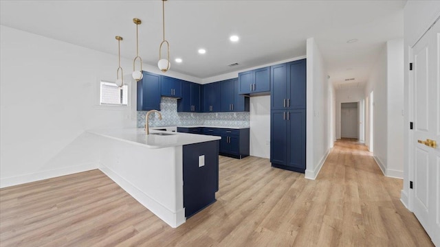 1072 Bruce St, Memphis, TN 38104 - kitchen featuring decorative light fixtures, kitchen peninsula, blue cabinets, light wood-type flooring, and backsplash
