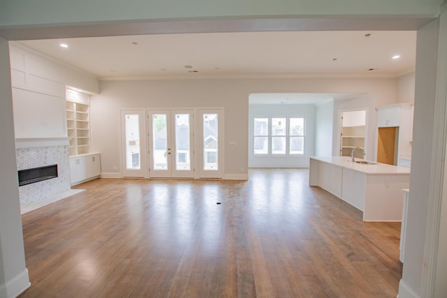 unfurnished living room with built in features, a healthy amount of sunlight, a tile fireplace, and light wood-type flooring