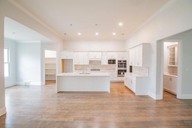 kitchen with stainless steel appliances, light hardwood / wood-style floors, tasteful backsplash, and an island with sink