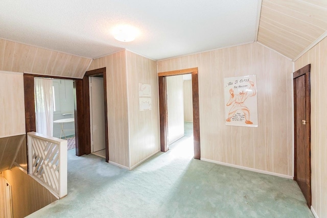 carpeted spare room with wooden walls, a textured ceiling, and vaulted ceiling