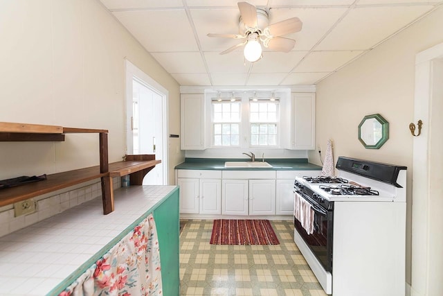 kitchen featuring a drop ceiling, gas range gas stove, white cabinets, and sink