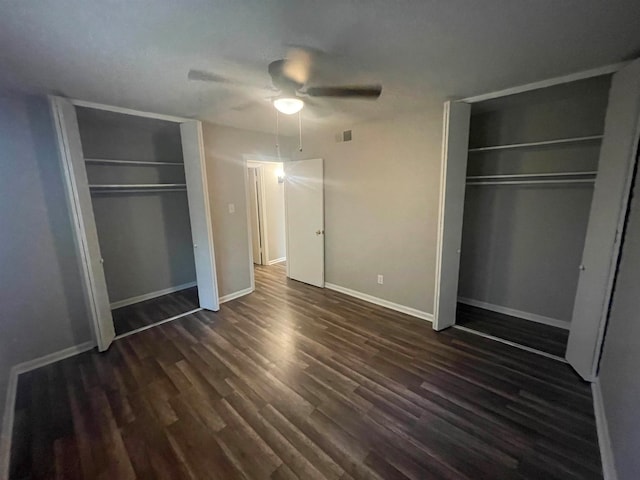 unfurnished bedroom with dark hardwood / wood-style flooring, ceiling fan, and two closets