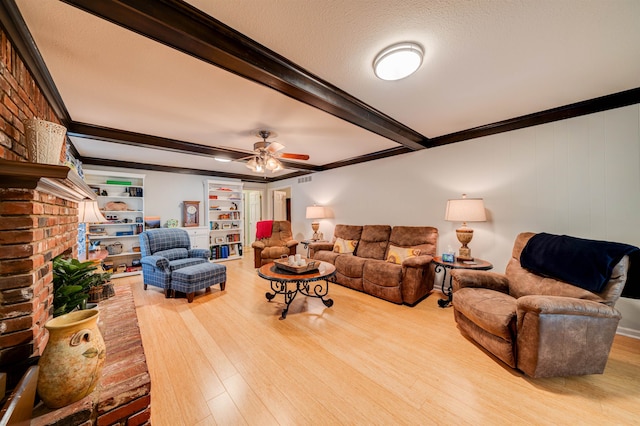 living room with a brick fireplace, light hardwood / wood-style flooring, ceiling fan, brick wall, and beamed ceiling