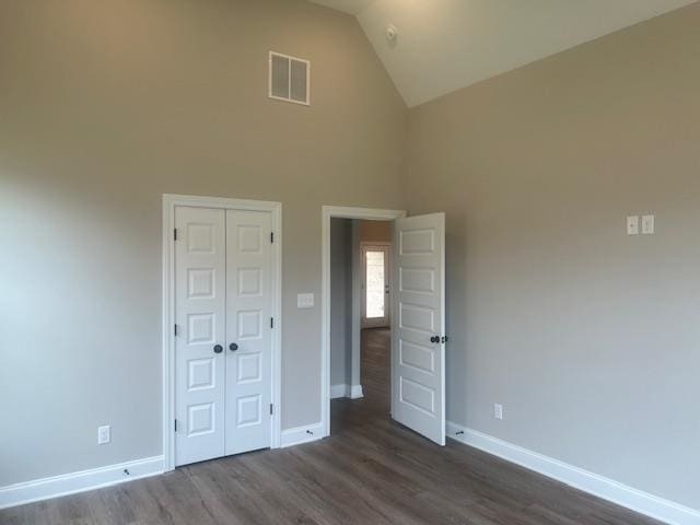 unfurnished bedroom with high vaulted ceiling, a closet, and dark hardwood / wood-style flooring