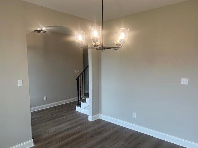 spare room featuring dark wood-type flooring and a notable chandelier