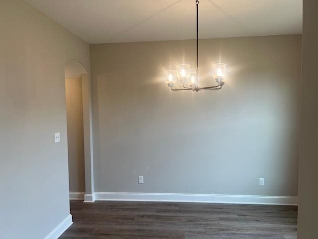 spare room featuring an inviting chandelier and dark wood-type flooring