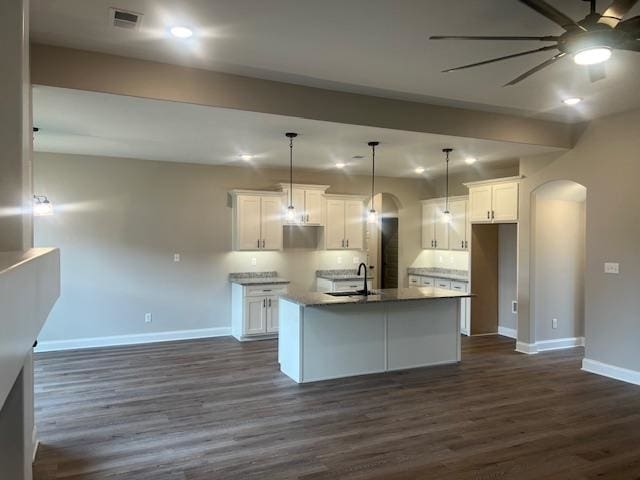 kitchen featuring dark wood-type flooring, white cabinets, ceiling fan, decorative light fixtures, and a kitchen island with sink