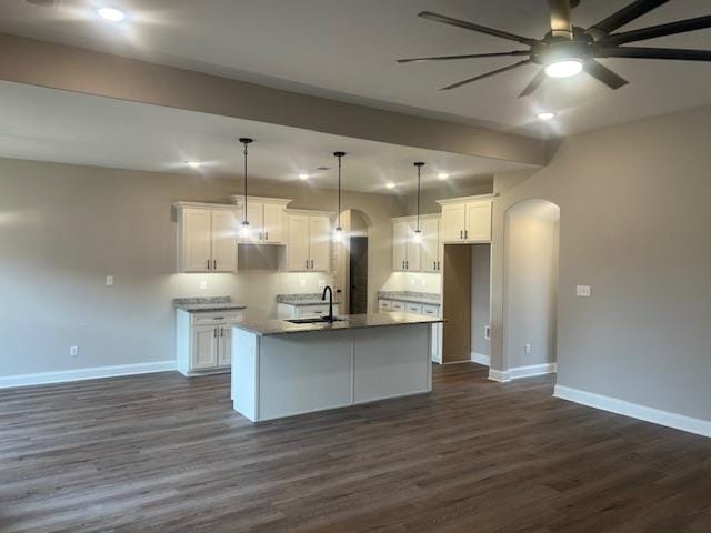 kitchen with pendant lighting, dark wood-type flooring, white cabinets, a center island with sink, and ceiling fan