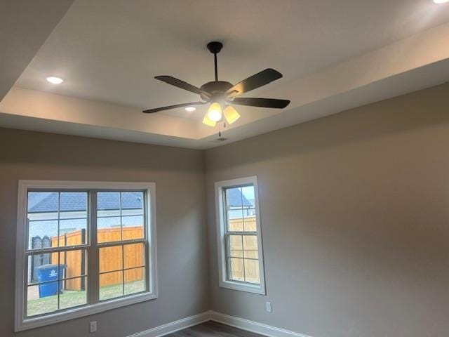 unfurnished room featuring a raised ceiling, ceiling fan, and plenty of natural light