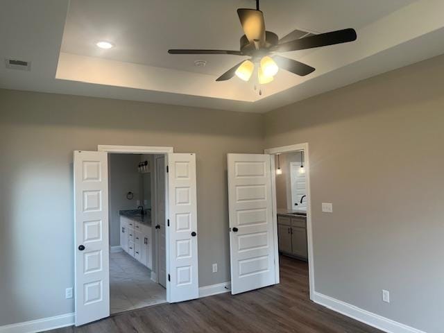 unfurnished bedroom with ceiling fan, sink, a tray ceiling, ensuite bath, and dark hardwood / wood-style flooring