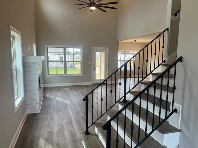 staircase featuring wood-type flooring, ceiling fan with notable chandelier, and a towering ceiling