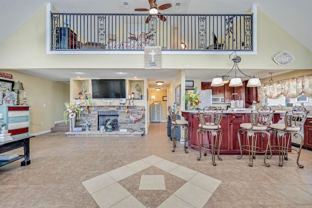 kitchen with decorative light fixtures, a high ceiling, light tile floors, a stone fireplace, and ceiling fan