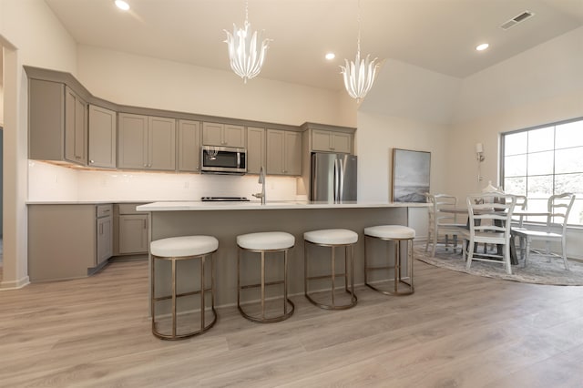 kitchen with an island with sink, stainless steel appliances, light hardwood / wood-style flooring, gray cabinets, and decorative light fixtures