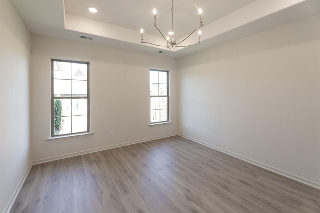 spare room with hardwood / wood-style flooring, an inviting chandelier, and a raised ceiling