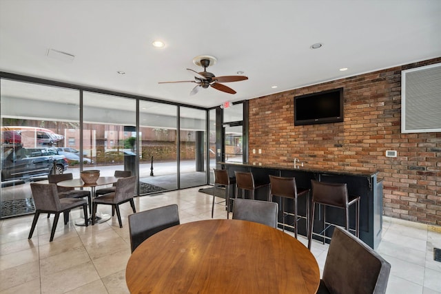 tiled dining room featuring a wealth of natural light, brick wall, ceiling fan, and a wall of windows