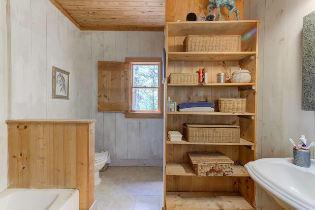 bathroom featuring wood walls, tile floors, wooden ceiling, a washtub, and toilet