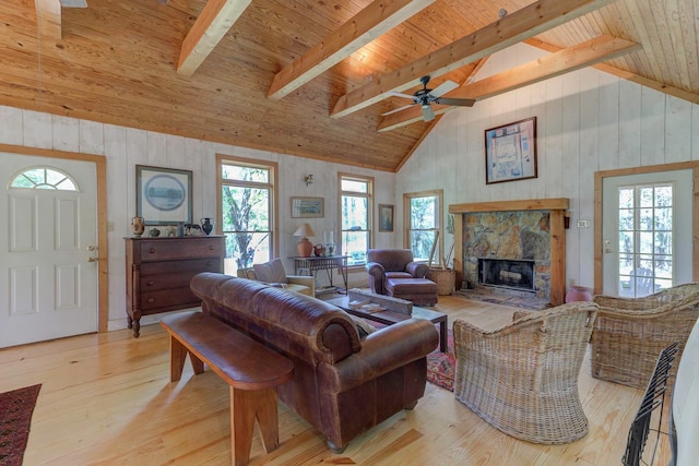 living room with a stone fireplace, ceiling fan, lofted ceiling with beams, wood ceiling, and light wood-type flooring