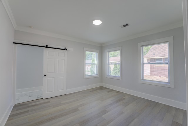 unfurnished bedroom featuring light hardwood / wood-style flooring, ornamental molding, and a barn door