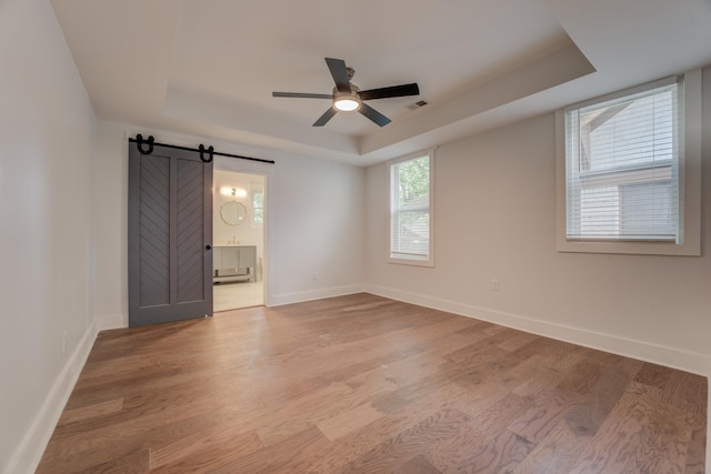 spare room featuring light hardwood / wood-style flooring, ceiling fan, a tray ceiling, and a barn door