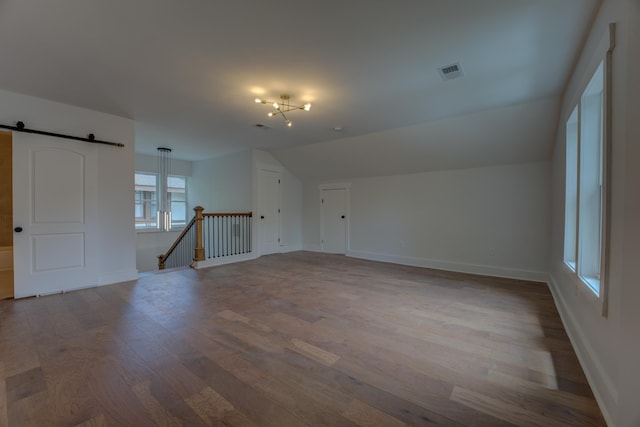 interior space with vaulted ceiling, a barn door, and hardwood / wood-style floors