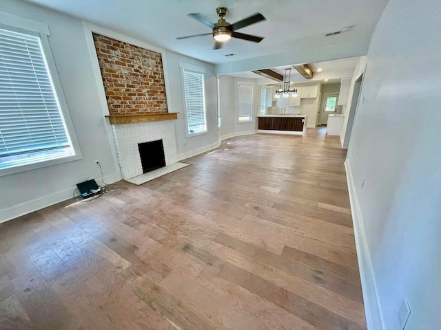 unfurnished living room featuring ceiling fan, a brick fireplace, hardwood / wood-style floors, brick wall, and a healthy amount of sunlight