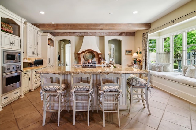 kitchen with light stone counters, beam ceiling, light tile floors, and stainless steel appliances