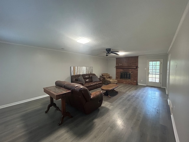 living room featuring ceiling fan, ornamental molding, a brick fireplace, a textured ceiling, and dark hardwood / wood-style floors