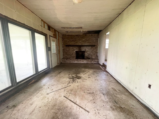 unfurnished living room featuring a wealth of natural light, concrete flooring, brick wall, and a fireplace