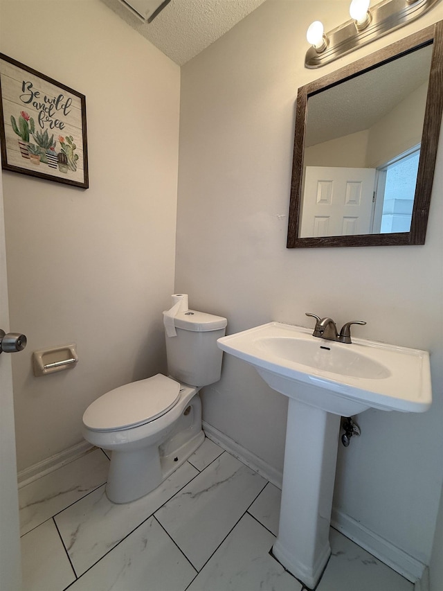 bathroom with marble finish floor, a textured ceiling, toilet, and baseboards