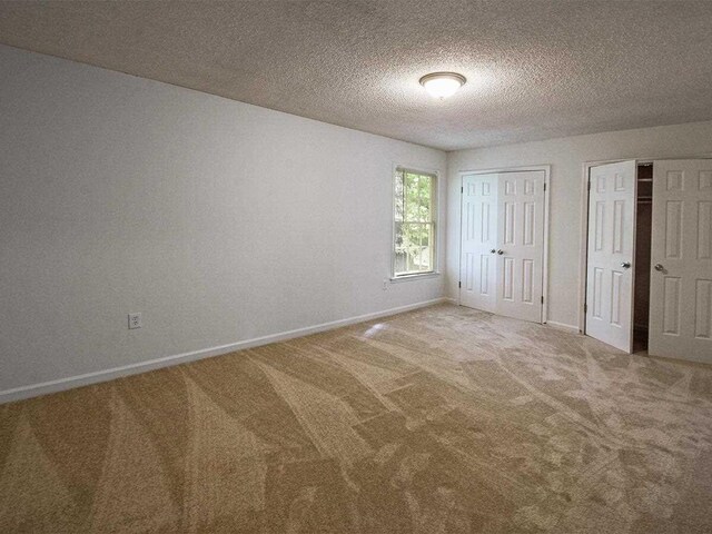 unfurnished bedroom featuring a textured ceiling, baseboards, two closets, and carpet