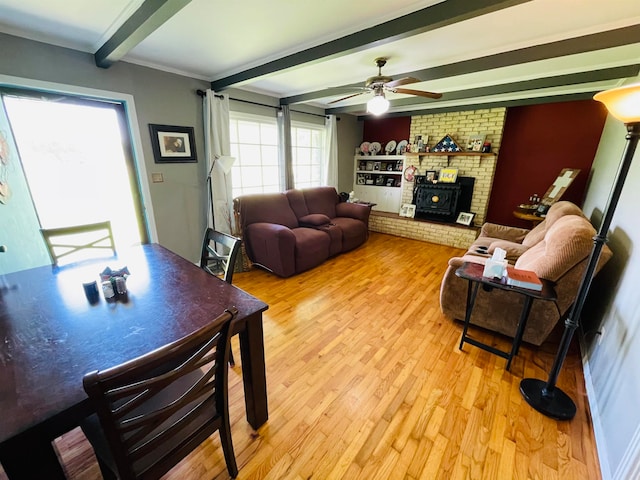 living room featuring ceiling fan, light hardwood / wood-style floors, beamed ceiling, and a brick fireplace